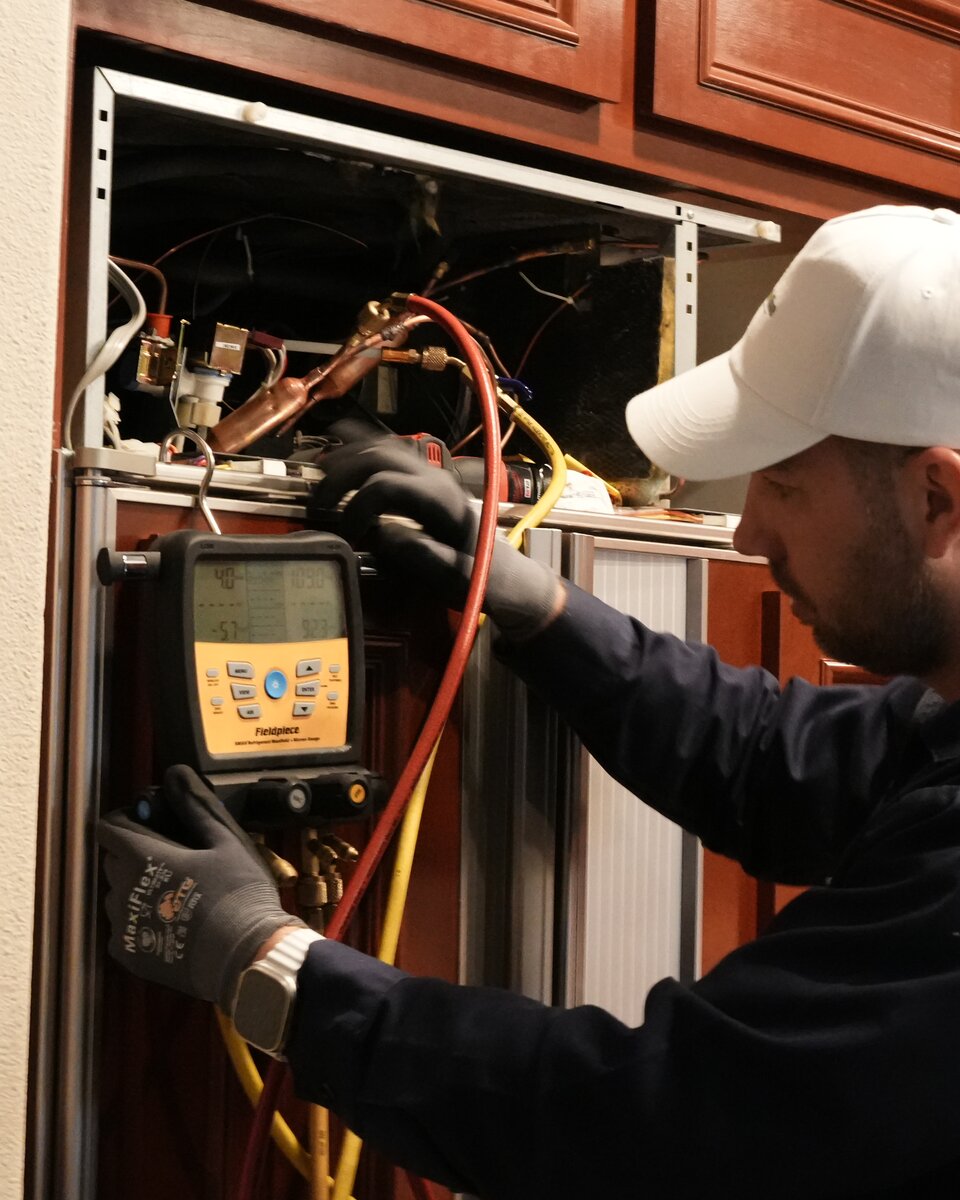 Peter, senior Sub-Zero specialist, running a refrigerant manifold diagnostic on an open built-in Sub-Zero sealed system in a premium cherry-cabinet kitchen